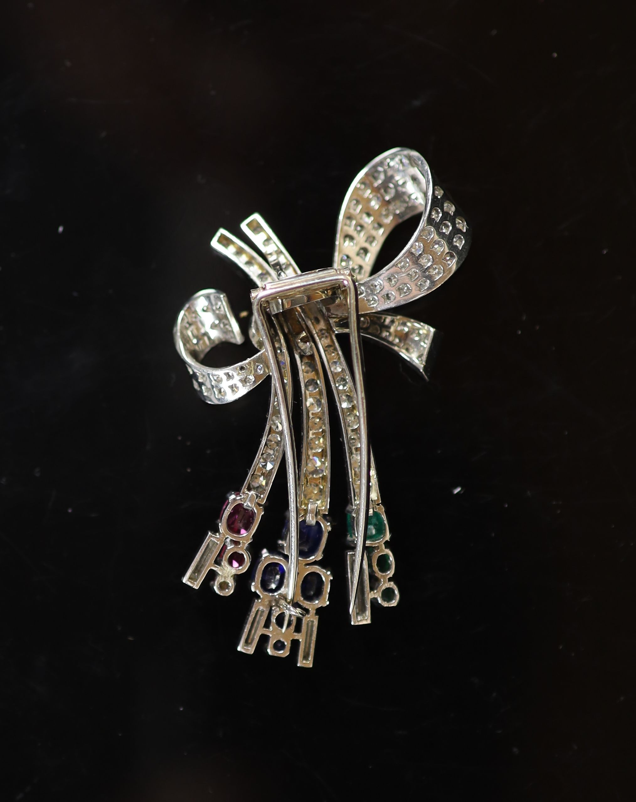 A mid 20th century Viennese platinum, ruby emerald, sapphire and diamond set stylised ribbon bow clip brooch